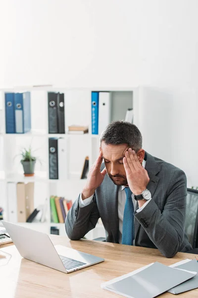 Hombre de negocios sentado en la mesa con el ordenador portátil y sensación de dolor de cabeza en la oficina - foto de stock