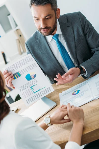 Enfoque selectivo del asesor guapo discutiendo documento con el inversor en el espacio de trabajo - foto de stock