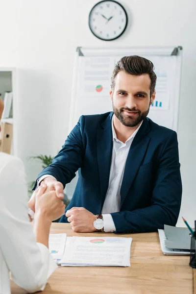 Handsome advisor in suit shaking hands with investor at workplace — Stock Photo