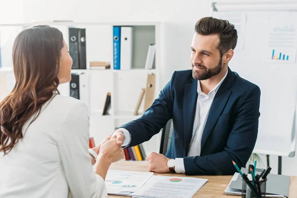 Asesor guapo en traje estrechando la mano con el inversor en el espacio de trabajo - foto de stock