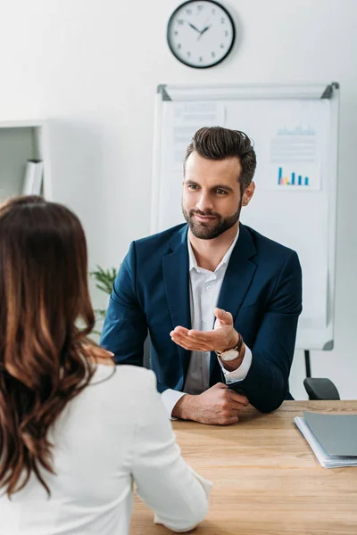 Selective focus handsome advisor in suit talking with beautiful investor at worplace — Stock Photo