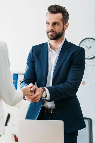 Asesor guapo en traje estrechando la mano con el inversor en el espacio de trabajo - foto de stock
