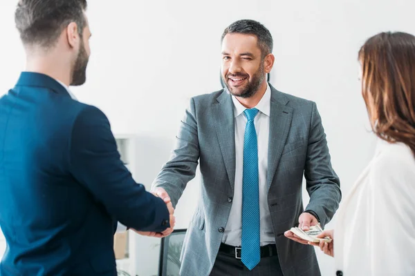 Selektiver Fokus des Beraters beim Händeschütteln mit Anlegern und beim Mitnehmen von Dollarnoten — Stockfoto