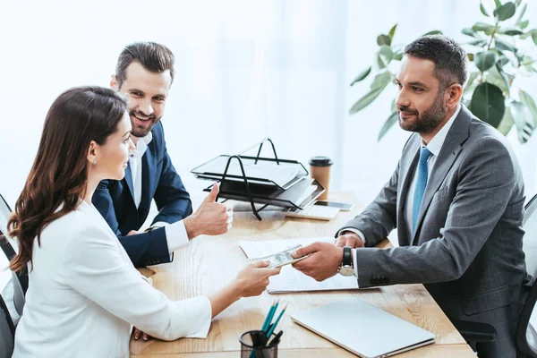 Investors in suits giving dollar banknotes to advisor at office — Stock Photo