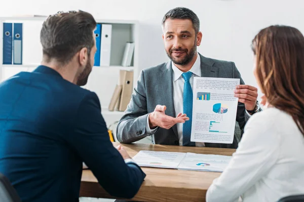 Selective focus of handsome advisor showing document to investors at workplace — Stock Photo