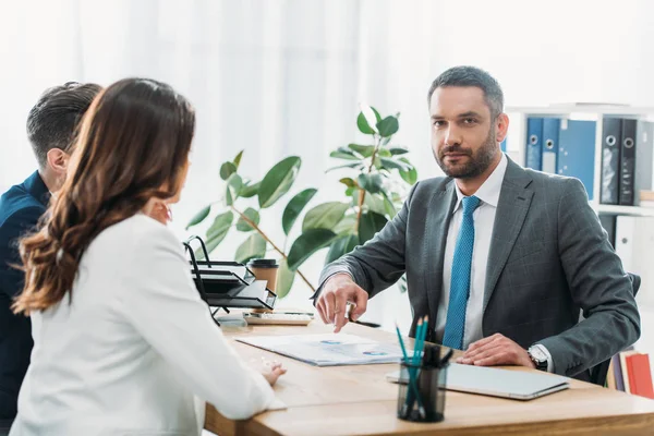 Selective focus of handsome advisor and investors in suits discussing document at office — Stock Photo