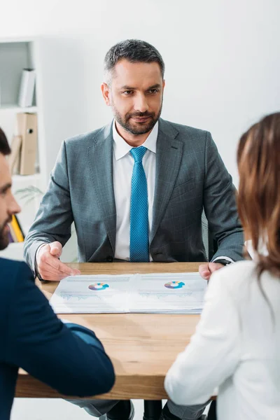 Selective focus of advisor in suit discussing documents with investors at office — Stock Photo