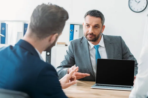 Selective focus of handsome advisor pointing with fingers at laptop with blank screen — Stock Photo