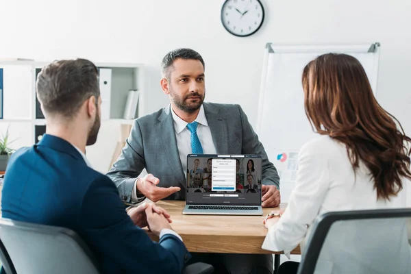 Asesor guapo enfoque selectivo apuntando con los dedos a la computadora portátil con linkedin sitio web en la pantalla - foto de stock