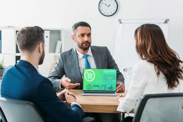 Selective focus of advisor pointing with fingers at laptop with shopping website on screen at workplace — Stock Photo