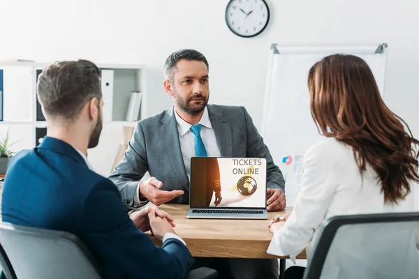 Selective focus of advisor pointing with fingers at laptop with tickets online website on screen at workplace — Stock Photo