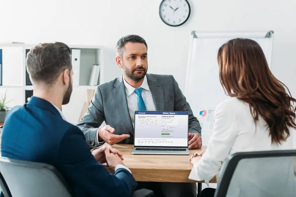 Selektiver Fokus des Beraters, der mit dem Finger auf Laptop zeigt, mit Facebook-Website am Bildschirm am Arbeitsplatz — Stockfoto