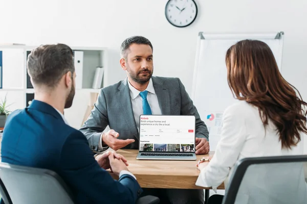 Selektiver Fokus des Beraters, der mit dem Finger auf den Laptop zeigt, mit Airbnb-Website am Bildschirm am Arbeitsplatz — Stock Photo