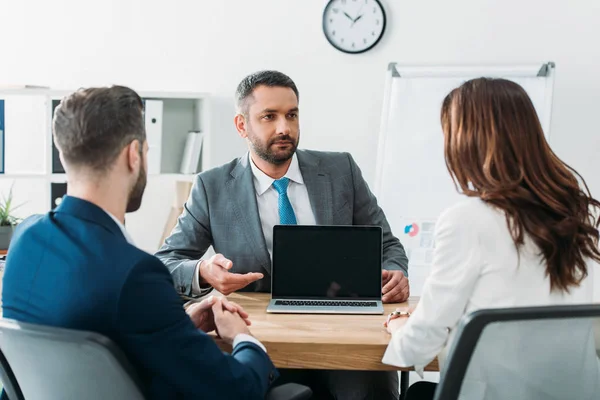 Selective focus of handsome advisor pointing with fingers at laptop with blank screen — Stock Photo