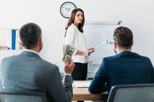 Selective focus of beautiful advisor holding document and investor holding dollar banknotes — Stock Photo