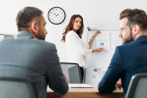 Selective focus of beautiful advisor holding document with investors on background — Stock Photo