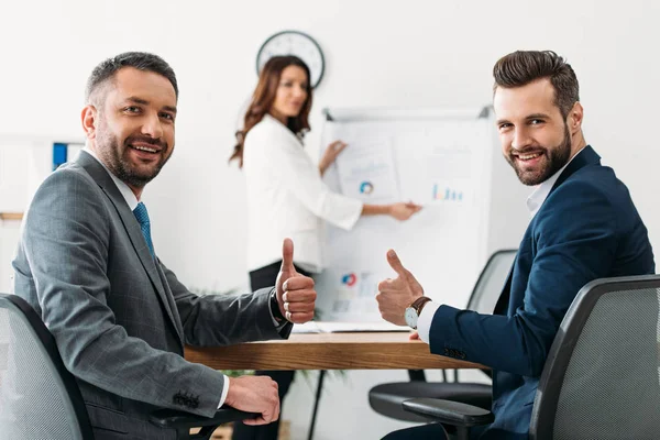 Selective focus of smiling investors with thumbs up at office — Stock Photo