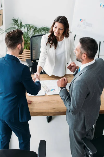 Beautiful advisor and handsome investor shaking hands at workplace — Stock Photo