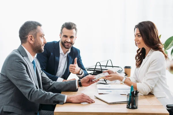 Handsome investor giving dollar banknotes to beautiful advisor — Stock Photo