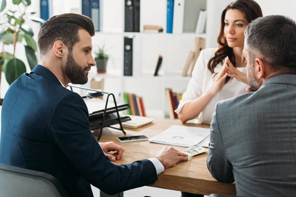 Selective focus of handsome investors in suits talking with attractive advisor at workspace — Stock Photo