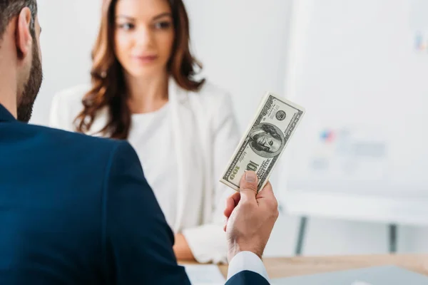 Selective focus of investor in suit holding dollar banknotes with advisor on background — Stock Photo