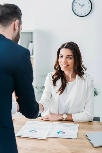 Selective focus of beautiful advisor shaking hands with investor at workplace — Stock Photo