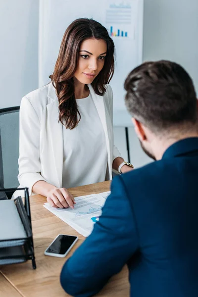 Selective focus of attractive advisor and investor in suits discussing document at office — Stock Photo