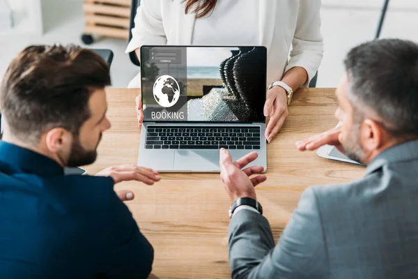 Selective focus of advisor showing to investors laptop with booking website on screen at workplace — Stock Photo