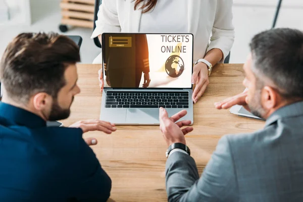 Selective focus of advisor showing to investors laptop with tickets online website on screen — Stock Photo