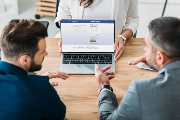 Selective focus of advisor showing to investors laptop with facebook website on screen — Stock Photo