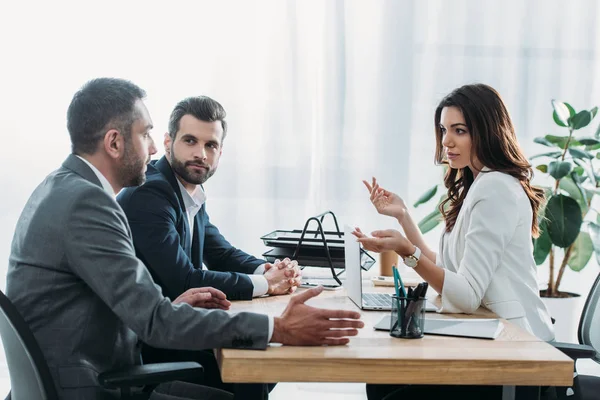 Hermoso asesor e inversores en trajes hablando en el lugar de trabajo - foto de stock