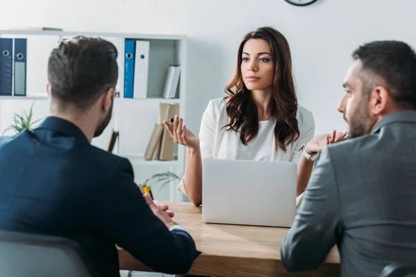 Selective focus of attractive advisor talking with investors in suits — Stock Photo