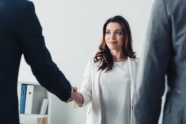 Foco seletivo do consultor em terno apertando as mãos com os investidores no espaço de trabalho — Fotografia de Stock