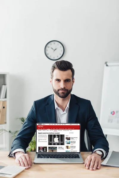 Handsome advisor in suit showing laptop with bbc news website on screen — Stock Photo