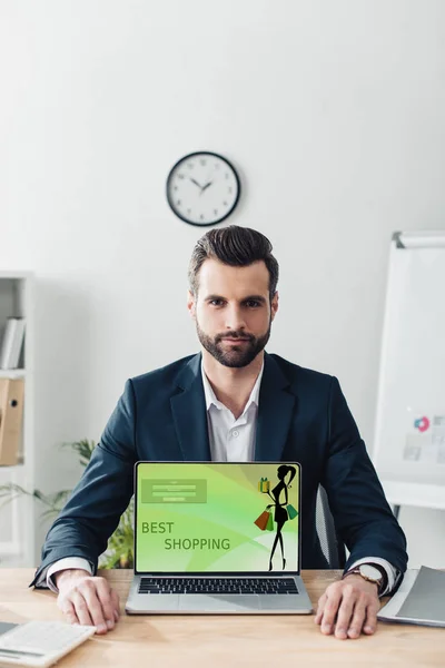 Schöner Berater im Anzug zeigt Laptop mit bester Shopping-Website auf dem Bildschirm — Stockfoto