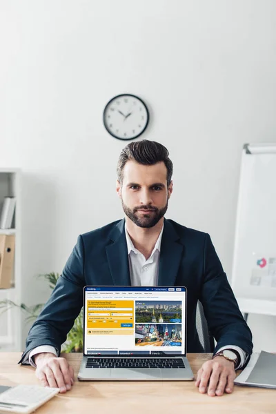 Schöner Berater im Anzug zeigt Laptop mit Buchungswebseite auf dem Bildschirm — Stockfoto