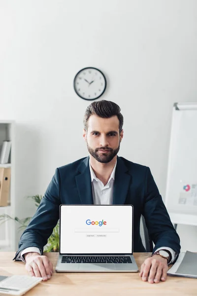 Asesor guapo en traje mostrando portátil con el sitio web de Google en la pantalla - foto de stock
