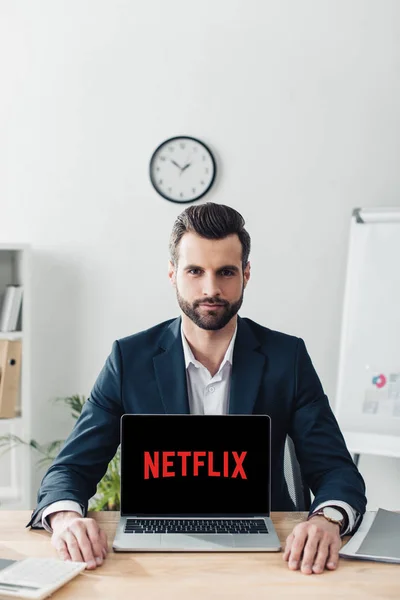 Bel consulente in giacca e cravatta che mostra computer portatile con sito web netflix sullo schermo — Foto stock
