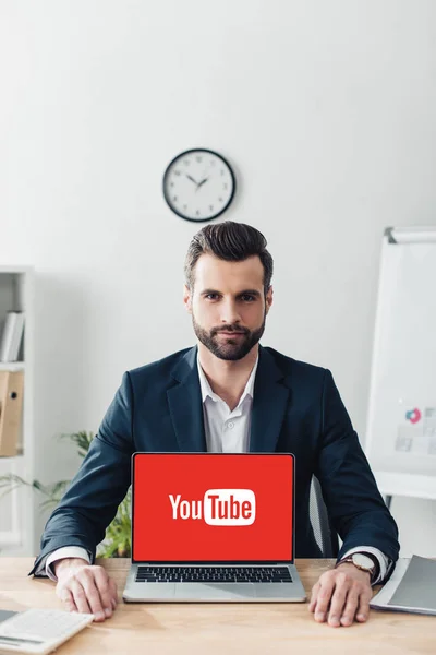 Красивый советник в костюме показывает ноутбук с YouTube сайт на экране — стоковое фото