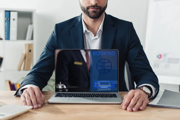Обрезанный вид советника в костюме показывающий ноутбук с бронированием веб-сайта на экране в офисе — стоковое фото