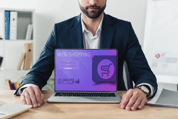 Vista ritagliata del consulente in giacca e cravatta che mostra laptop con sito web-shopping sullo schermo in ufficio — Foto stock