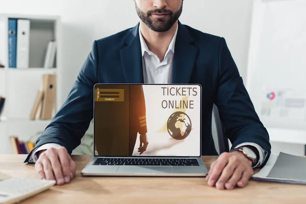 Cropped view of advisor in suit showing laptop with tickets online website on screen — Stock Photo