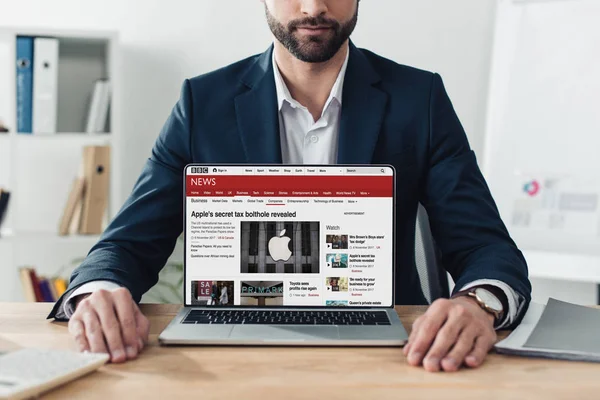 Vista recortada del asesor en traje que muestra el ordenador portátil con el sitio web de noticias de la penes en la pantalla en la oficina - foto de stock
