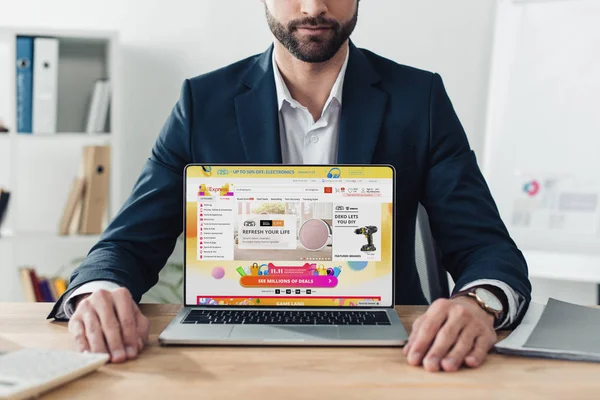 Cropped view of advisor in suit showing laptop with aliexpress website on screen at workplace — Stock Photo