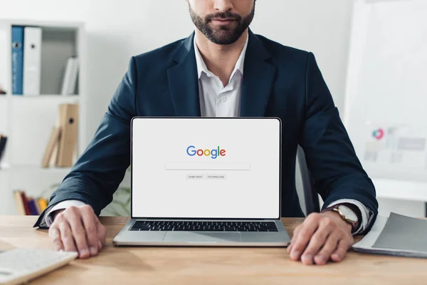 Cropped view of advisor in suit showing laptop with google website on screen at office — Stock Photo