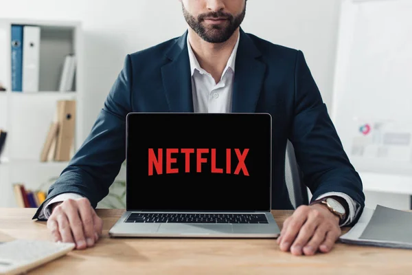 Vista recortada del asesor en traje que muestra el ordenador portátil con el sitio web de netflix en la pantalla - foto de stock