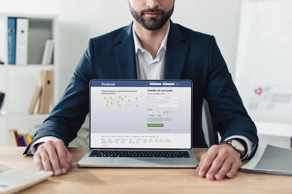 Vista cortada de conselheiro em terno mostrando laptop com site do facebook na tela — Fotografia de Stock
