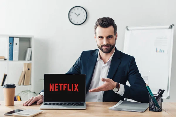 Handsome advisor in suit pointing with fingers at laptop with netflix website on screen at office — Stock Photo