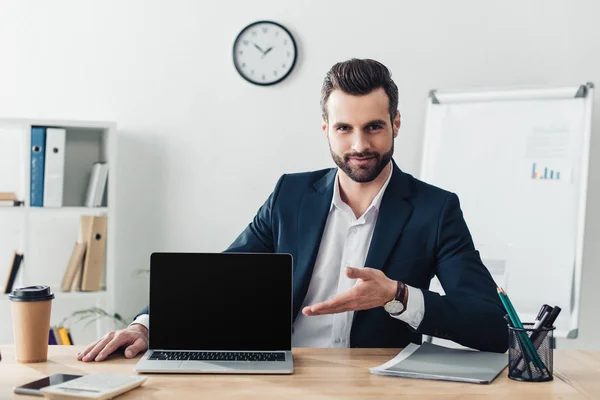 Schöner Berater im Anzug zeigt mit den Fingern auf Laptop mit leerem Bildschirm im Büro — Stockfoto