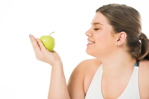 Молодая улыбающаяся толстая женщина смотрит на зеленое яблоко, изолированное на белом — стоковое фото